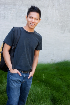 young male asian student standing outside with backpackの写真素材