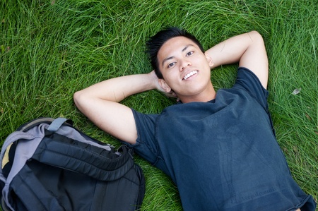 young male asian student lying in the grass with a backpackの写真素材