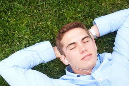 young man lying in grass listening to musicの写真素材