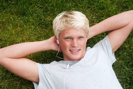 young teenager lying in grass listening to musicの写真素材