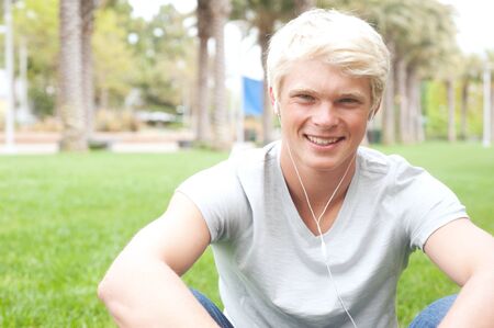 portrait of a young teenage boy sitting in the grass listening to musicの写真素材