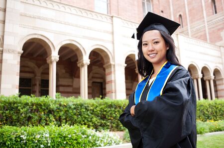 portrait of a beautiful young asian woman in graduation cap and gown standing outside on campusのeditorial素材