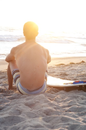 surfer sitting on the beach during sunsetの写真素材