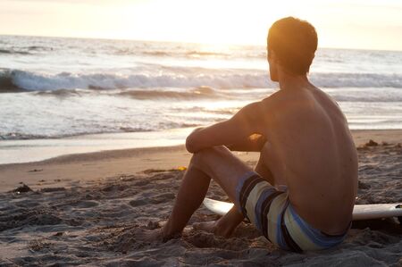 surfer sitting on the beach during sunsetの写真素材