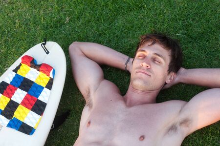 portrait of an active young man lying in the grass with surfboardの写真素材