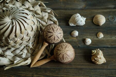 Vacation souvenirs. Hat and maracas from palm leaves and sea shells on brown wood background