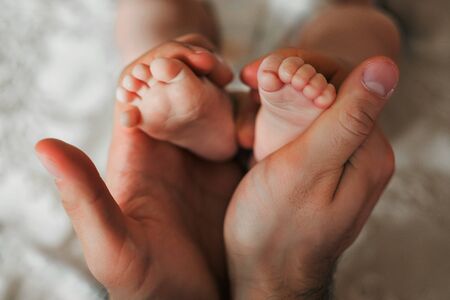 The legs of a newborn baby in the hands of his father
