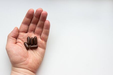 Several brown pills in a male hand on a white background with copyspaceの写真素材