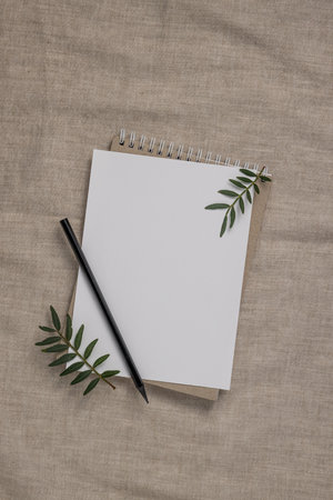 Summer wedding stationery mock-up scene. Blank greeting card, craft paper envelope and green branches on linen textile background. Feminine Mediterranean top view, flat lay.の写真素材