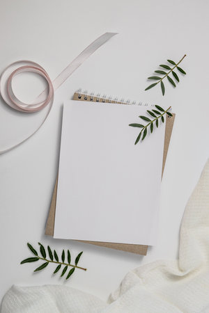 Summer wedding stationery mock-up scene. Blank greeting card, craft paper envelope and pink ribbon isolated on white table background. Feminine Mediterranean top view, flat lay.の写真素材