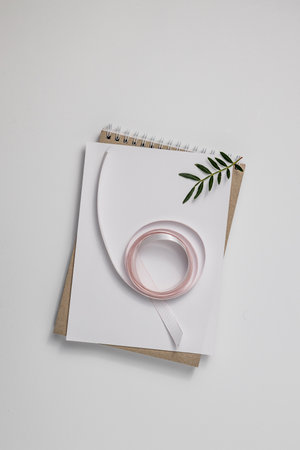 Summer wedding stationery mock-up scene. Blank greeting card, craft paper envelope and pink ribbon isolated on white table background. Feminine Mediterranean top view, flat lay.の写真素材