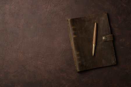 brown leather diary and pen on brown background or table with copy spaceの写真素材