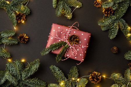 gift box decorated on a black background with a garland of fir branches and conesの写真素材