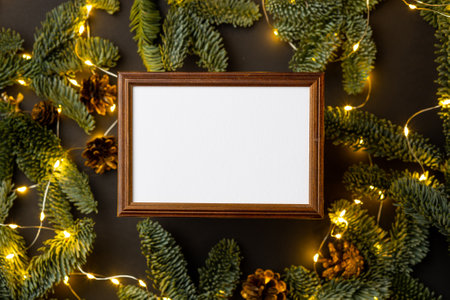 Empty brown wooden border with garland of fir branches and cones and lights on a black background.の写真素材