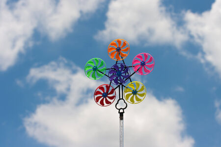 Colorful pinwheel against blue sky with cloudsの写真素材