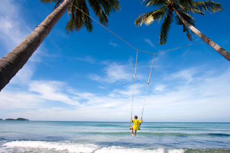 Boy swing between trees near the seaの写真素材