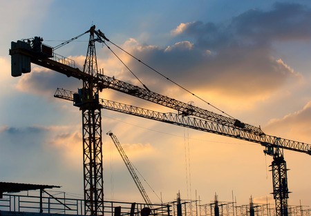 Industrial construction cranes silhouettes over sunset.