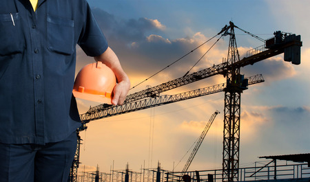 engineer holding orange helmet on background of new office buildings, Silhouette Crane and...