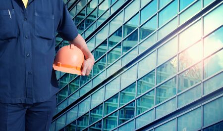 engineer holding orange helmet for workers security on office buildings in blue color tone