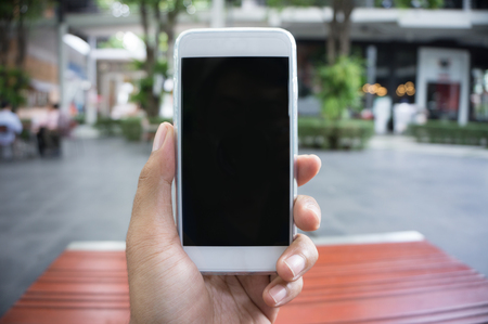 Man's hand shows mobile smartphone in vertical position, blurred background - mockup templateの写真素材