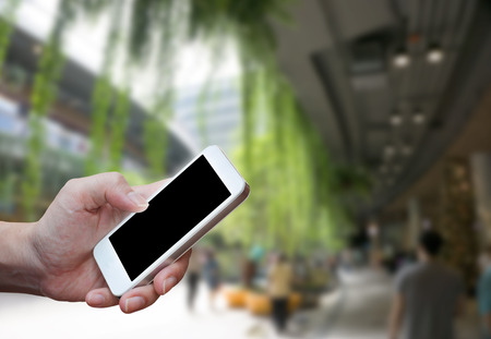 Man's hand shows mobile smartphone in vertical position, blurred background - mockup templateの写真素材