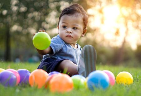 Cute asian baby playing colorful ball in green grass - Sunset filter effectの写真素材