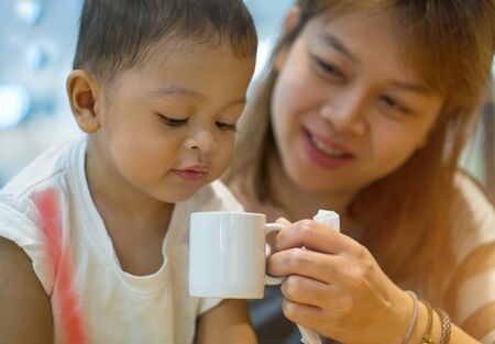 Asian mother and son. The mother was raised a white cup of water. His son drinking the waterの写真素材