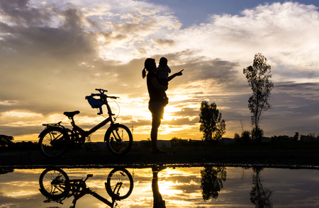 Reflection Silhouette of mother with her toddler against the sunset and bicycle. Asian family activity lifestyle.の写真素材