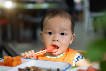Asian baby girl in restaurant with a spoon eats food.の写真素材