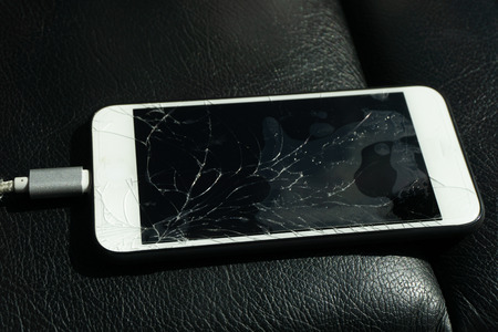 Close up of cracked smartphone screen lay on black leather.の写真素材