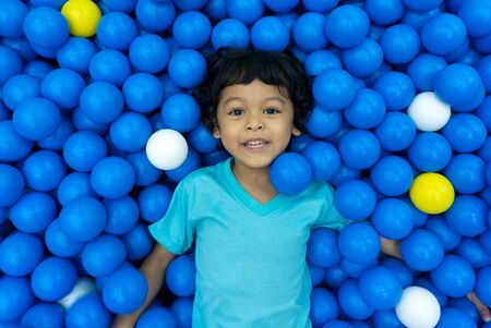 A little Asian boy is playing with a lot of blue and yellow balls. And eyes looking at the camera...