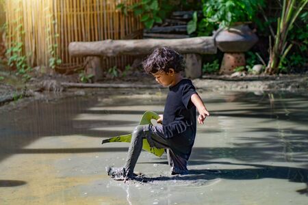 1 Asian boy playing with mud in a fun place inside a mud pit built for children to play together.