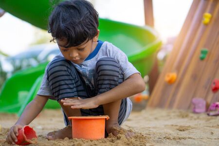 An Asian boy is playing, digging sand in the playground.の写真素材