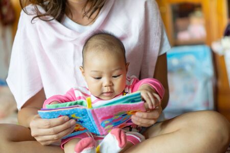 A 6-month-old Asian girl sat on the mother's lap and reading a children's story book.の写真素材