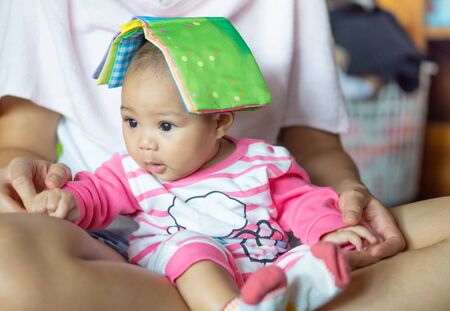 A 6-month-old Asian girl was sitting on the mother's lap. And there is a story book for children on...