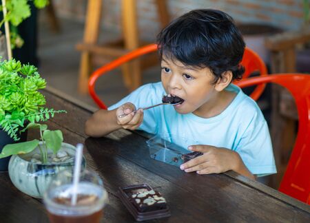 Asian boy is eating brownies on a wooden table during the day time.の写真素材