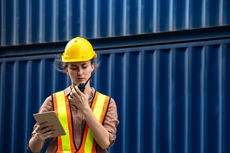 Female foreman is using walkie talkie and computer tablet to control work in industrial businessの写真素材