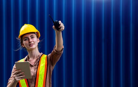 Female foreman is using walkie talkie and computer tablet to control work in industrial businessの写真素材