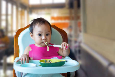An Asian girl, 11 months old, is eating food on baby table food.の写真素材