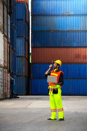 industrial worker is controlling container loading by walkie talkie and computer laptop in import-export business.の写真素材