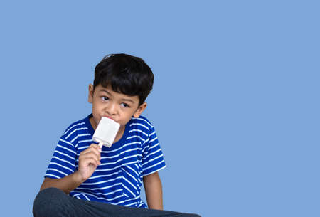 Little Thai boy eating white chocolate Ice cream Isolated over blue backgroundの写真素材
