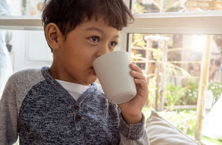 An Asian boy thirsty drinking water from a white plastic cup.