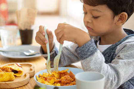 The child eats an omelet wrapped in fried rice with bacon sauce inside.の写真素材
