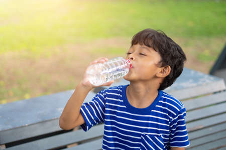 Asian kid thirsty water and drinking water from a transparent plastic bottle in the park.の写真素材