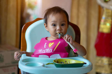 Asian baby girl 11 months year old is eating food on baby table food.の写真素材