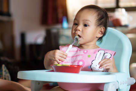 Asian baby girl 11 months year old is eating food on baby table food.の写真素材