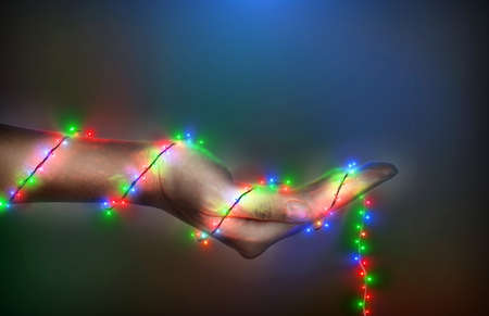 A Woman hand and multicolored Christmas lights are wrapped around hands on the dark. Christmas and...