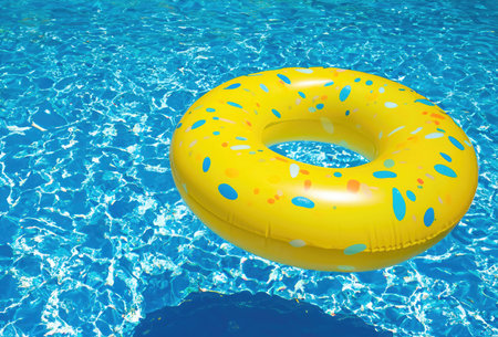 Yellow Swimming Pool Ring Float in Vibrant Blue Water" - Experience the essence of summer with this delightful image capturing a yellow swimming pool ring float gently floating on the vibrant blue water.の素材