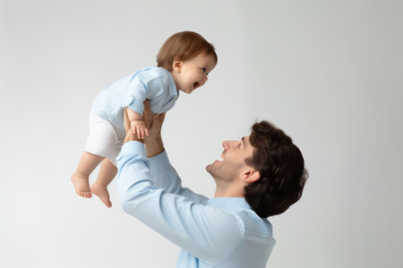 "Dad Lifting Baby with Joy - A heartwarming moment as a young father lifts his baby overhead."の素材