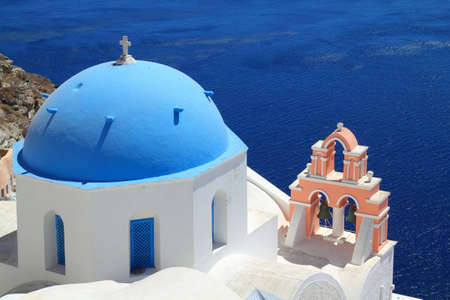 A church with a blue dome overlooks the spectacular caldera surrounding the beautiful island of Santorini, Greece の写真素材
